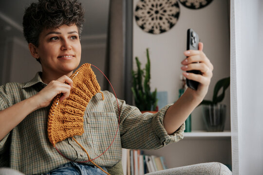 Woman knitting with warm wool and taking a selfie at home