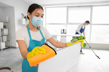 Female Asian janitor with mask cleaning computer monitor in office