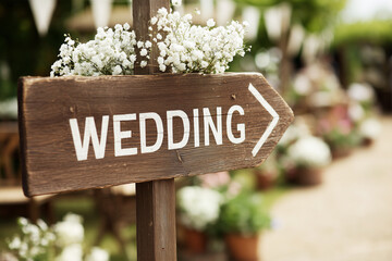 Wedding rustic wood direction sign with white flowers in a garden, country vibes bohemian rural chic wedding party