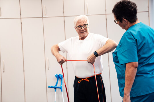 Man exercising with resistance band under supervision in physiotherapy
