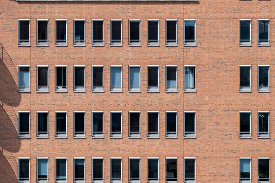 Urban brick architecture facade with windows showing symmetry pattern and texture in minimal geometric structure with clean daylight exterior repetition