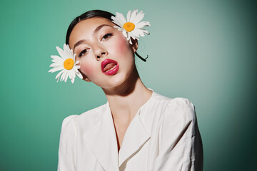 Creative beauty portrait of a young woman with bold makeup and daisy accessories touching her...