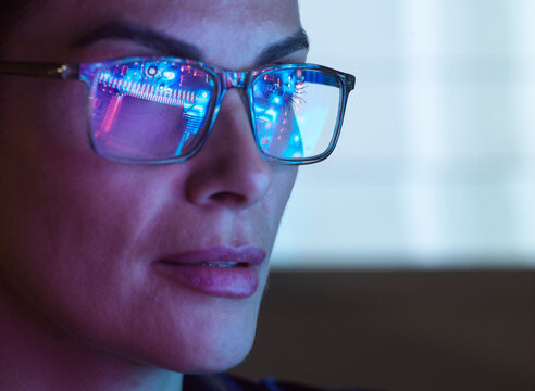 Woman with glasses reflecting computer chips and data screen in tech setting