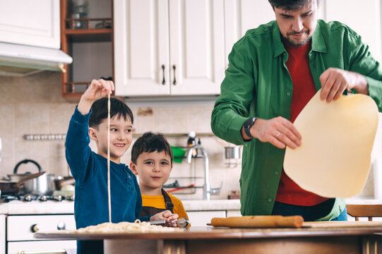 Father cooking with sons in kitchen making homemade noodles