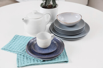 Different clean dishes and teapot on white table in kitchen