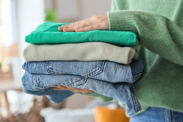 Young woman holding stack of clean clothes at home, closeup
