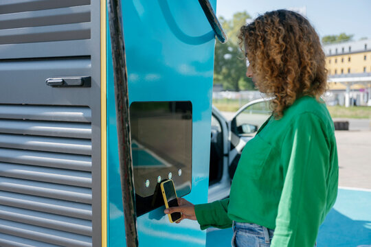 Woman paying for electric car charging at station with mobile phone