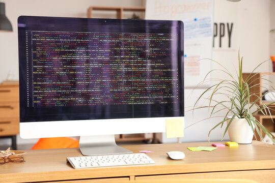 Computer monitor with code and plant on programmer's desk in office