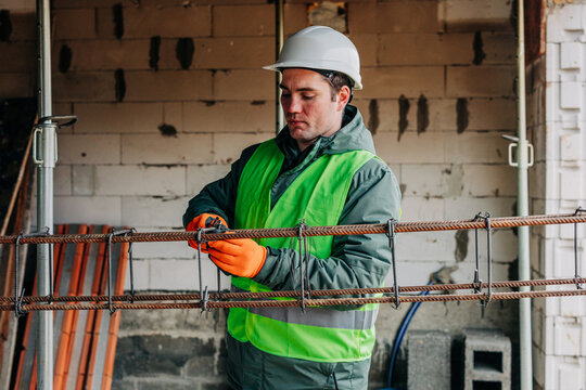 Builder in hard hat twisting reinforcement at construction site