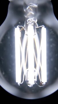 Close-up of a modern filament light bulb glowing brightly against a dark