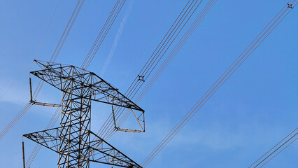 Tall steel lattice transmission tower stands against a clear bright blue sky supporting high voltage power lines © AmjadRosli