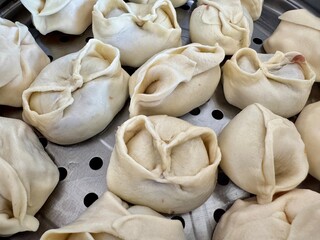 A close-up shot of freshly prepared traditional manty dumplings arranged in a metal steamer tray, showcasing authentic Central Asian culinary heritage.