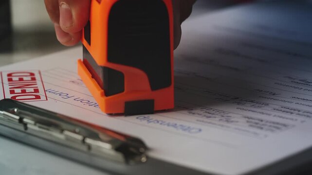 Close-up of hand putting multiple denied stamps on citizenship application form