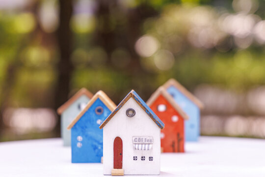 Miniature wooden houses in various colors are arranged on white surface with blurred green background, creating whimsical and charming scene