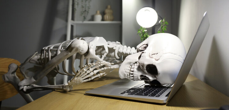 Human skeleton model lying on laptop in office at night