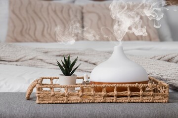 Wicker tray with air humidifier, houseplant and essential oil in bedroom