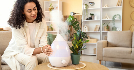 Young African-American woman with air humidifier on table at home