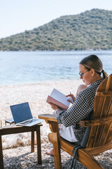 Digital nomad working on laptop at beach lounge, portable solar panel charger on table, remote work...