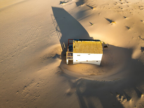 Costa da Caparica, Portugal - 31 January 2025: Aerial view of a white building casting a long shadow on the warm-toned sand, creating a striking contrast.