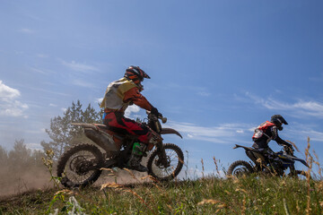 Obraz premium Two motocross riders racing side by side on grassy hillside dirt track, kicking up dust under