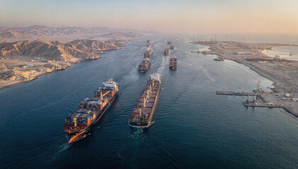 Convoy of large cargo and container ships navigate narrow waterway