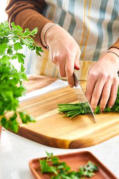 woman hands chopping parsley with a knife on a cutting board in a kitchen setting
