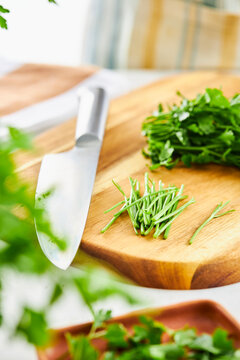 Chopped parsley stems on a cutting board with a knife beside them on a kitchen setting