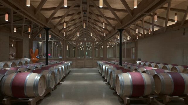 Chateau de Malleret, France - 06 January 2026: Aerial view of rows of wine barrels with red tops under a wooden ceiling in a cellar, creating a warm ambiance.