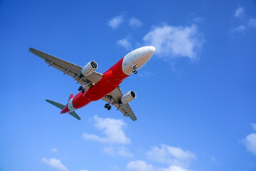 Obraz premium A red passenger jet streaks through a cloud covered sky before landing low overhead.