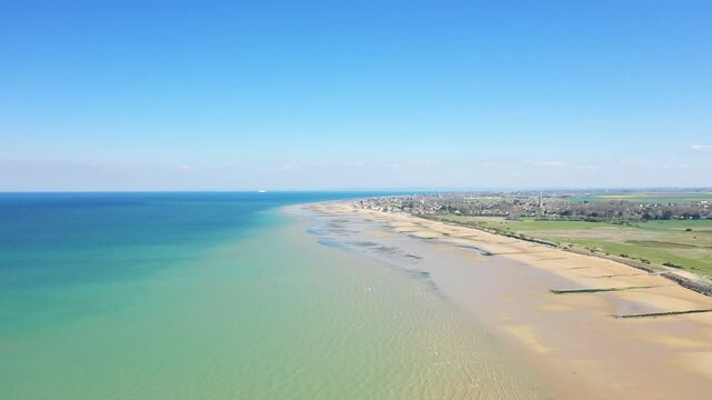 Wide aerial shot of the sandy shoreline and turquoise waters at Juno Beach near Bernieres sur Mer, Normandy, France, under a clear blue sky.