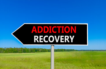 Addiction recovery symbol. Concept words Addiction recovery on beautiful black road sign. Beautiful blue sky green grass field background. Psychology addiction recovery concept. Copy space.