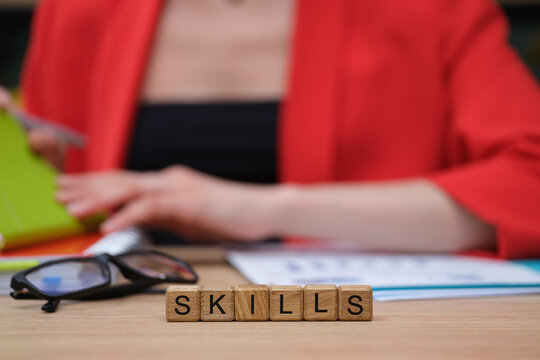 A person in a striking red jacket works diligently at a desk, surrounded by colorful materials, focusing on developing skills with wooden blocks spelling SKILLS.