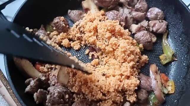 Stirring homemade rustic Mediterranean fresh seasoned diced lamb and couscous in hot steaming pan