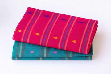 Close-up of two folded traditional cotton sarees in magenta and teal blue with heart patterns. Isolated on white background, perfect for South Asian ethnic wear and fashion concepts
