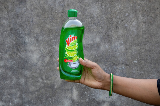 Hand of a housewife holding a plastic bottle of concentrated dish soap with lemon fragrance. Professional cleaning equipment for sanitary kitchen, hygiene routine, and household utility.