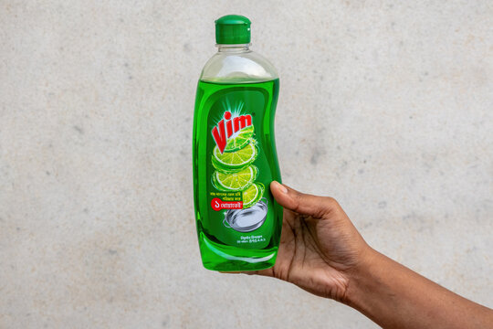 Close-up of a woman hand holding a bottle of vim lemon dishwashing liquid soap against a plain wall. Household cleaning product, liquid detergent for kitchen utensils, and hygiene concept.