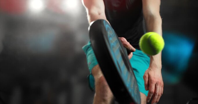 Super slow motion close-up of a padel player hitting a ball with a racket, filmed at 1000 fps. Dramatic studio lighting highlights the impact, motion and energy of the sport in a dynamic action
