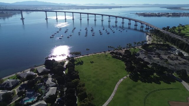 Bridge and marina sweep captures Coronado Bridge curving above San Diego Bay beside Tidelands Park. Warm reflections highlight sailboats, smooth water gradients, crisp shoreline, Coronado, CA