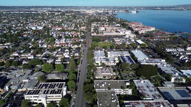 Bayfront neighborhood view frames Tidelands Park beside Mullinex Dr near Coronado Bridge. Soft coastal light reveals textured roofs, bright turf, and layered palms across Coronado, California