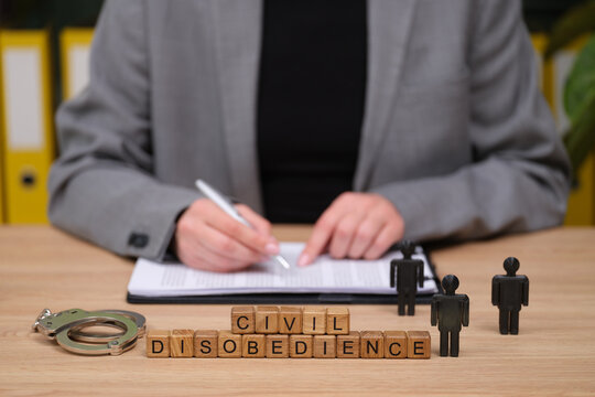 A focused individual in a stylish gray blazer writes notes while surrounded by wooden blocks spelling civil disobedience.