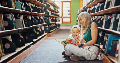 Fototapeta premium Grandmother, reading book and girl in library, smile and bonding together for child development. Senior woman, kid or family on floor, happiness and support for education, literacy, hobby or teaching
