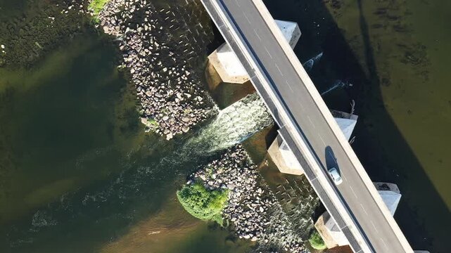 Drone shot of a modern bridge crossing the Loire river in La Charite sur Loire, France, with water flowing beneath and rocks lining the riverbanks.
