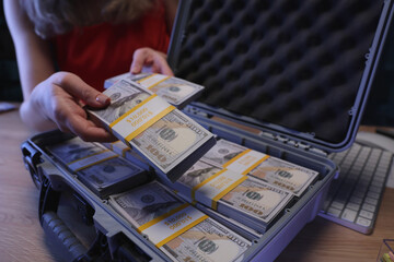 A person delicately handles stacks of money inside a secure briefcase, creating an air of mystery and intrigue. The scene unfolds under dim lighting, highlighting the cash s crisp details. © H_Ko