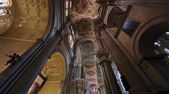 Historic Malaga cathedral interior featuring colorful stained glass windows, lavish carved ceiling decoration and towering stone columns, Spain