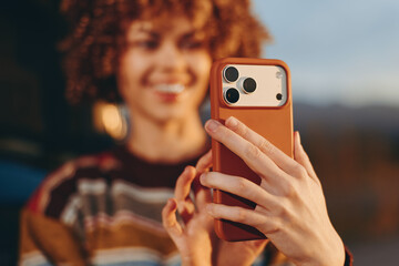 Smiling woman wearing rainbow sweater taking selfie with smartphone outdoors, natural light...