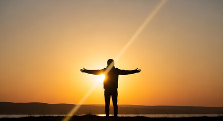 Fototapeta premium Man standing with arms outstretched at sunset by the sea 