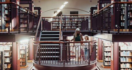 Happy, grandma and holding hands with child in library for education, learning or literature....
