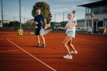 Obraz premium Tennis coach teaching young girl forehand on clay court