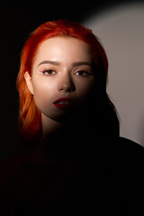 Fototapeta premium Captivating portrait of a stylish young woman with vibrant red hair in soft lighting