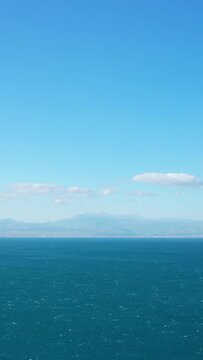 Wide view of deep blue sea with distant mountains under a clear sky near Corinth, Greece. Tranquil seascape with a few scattered clouds.